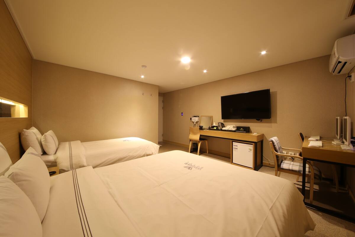 Une chambre d’hôtel avec deux lits, un bureau, une chaise, une télévision et un appareil de climatisation.
