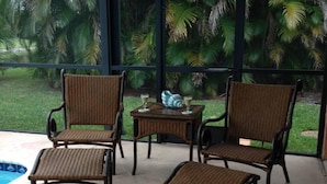Eine Terrasse mit Korbstühlen, einem kleinen Tisch, einem Getränk und Blick auf einen Swimmingpool und Palmen.