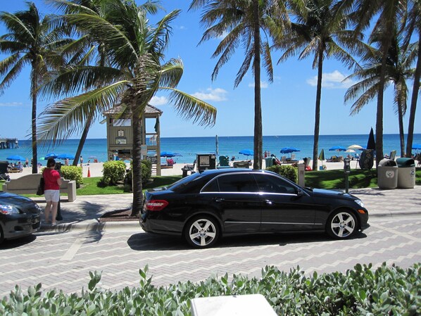 A black car parked on a paved area with palm trees and a lifeguard tower in the background. - Comfortable 3-bedroom waterfront villa with heated pool (Deerfield)
