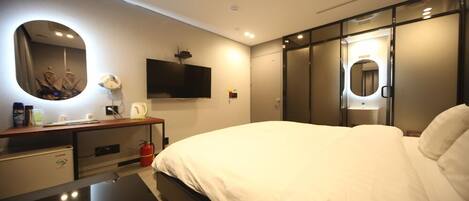 Una habitación de hotel moderna con una cama grande, una mesita de noche con lámpara, un televisor y un armario con espejo.
