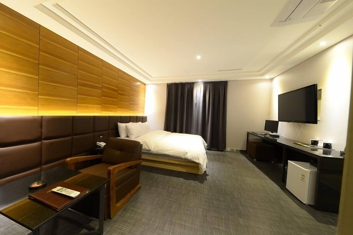 A hotel room with a bed, a sofa, a desk, a television, and a minibar.