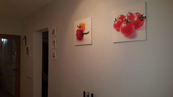 A hallway with framed pictures on the wall, a door, and a mirror.