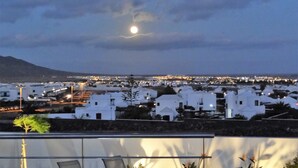 A terrace with outdoor seating and a view of a town with white buildings under a night sky with a visible moon. - Villa with private heated pool and jacuzzi (PLAYA BLANCA)