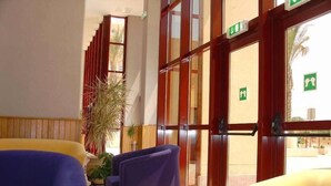 A hotel lobby with a reception desk, a large potted plant, and a view of the outside.