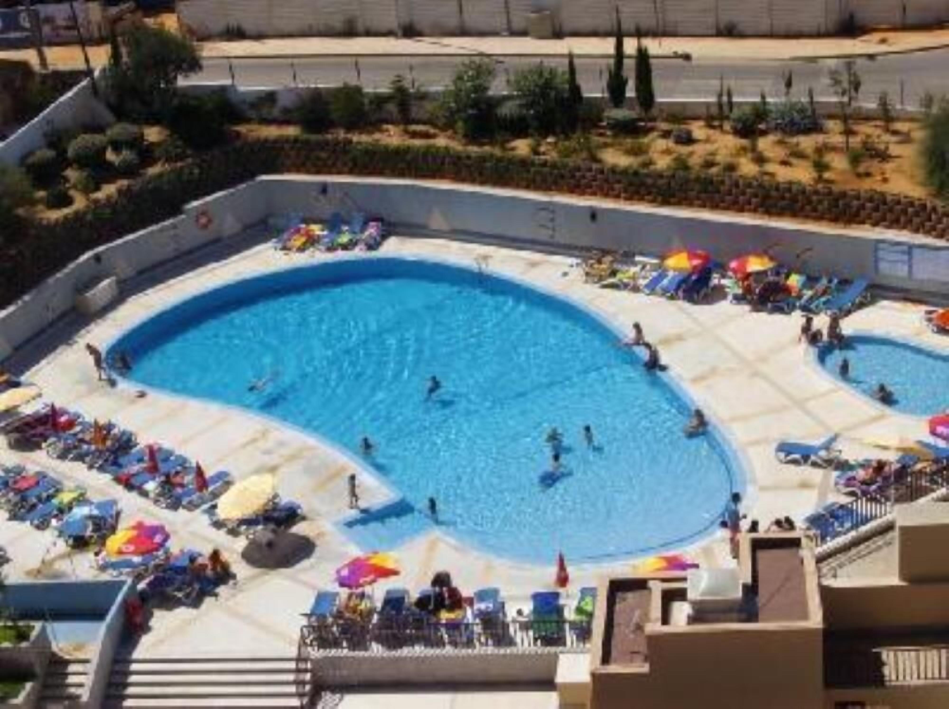En stor udendørs swimmingpool med flere baner, omgivet af liggestole og parasoller.