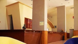 A reception area with a wooden reception desk, yellow and blue seating, and a tiled floor.