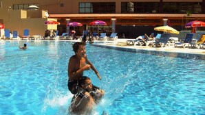 A swimming pool with lounge chairs and umbrellas, surrounded by a building with balconies.