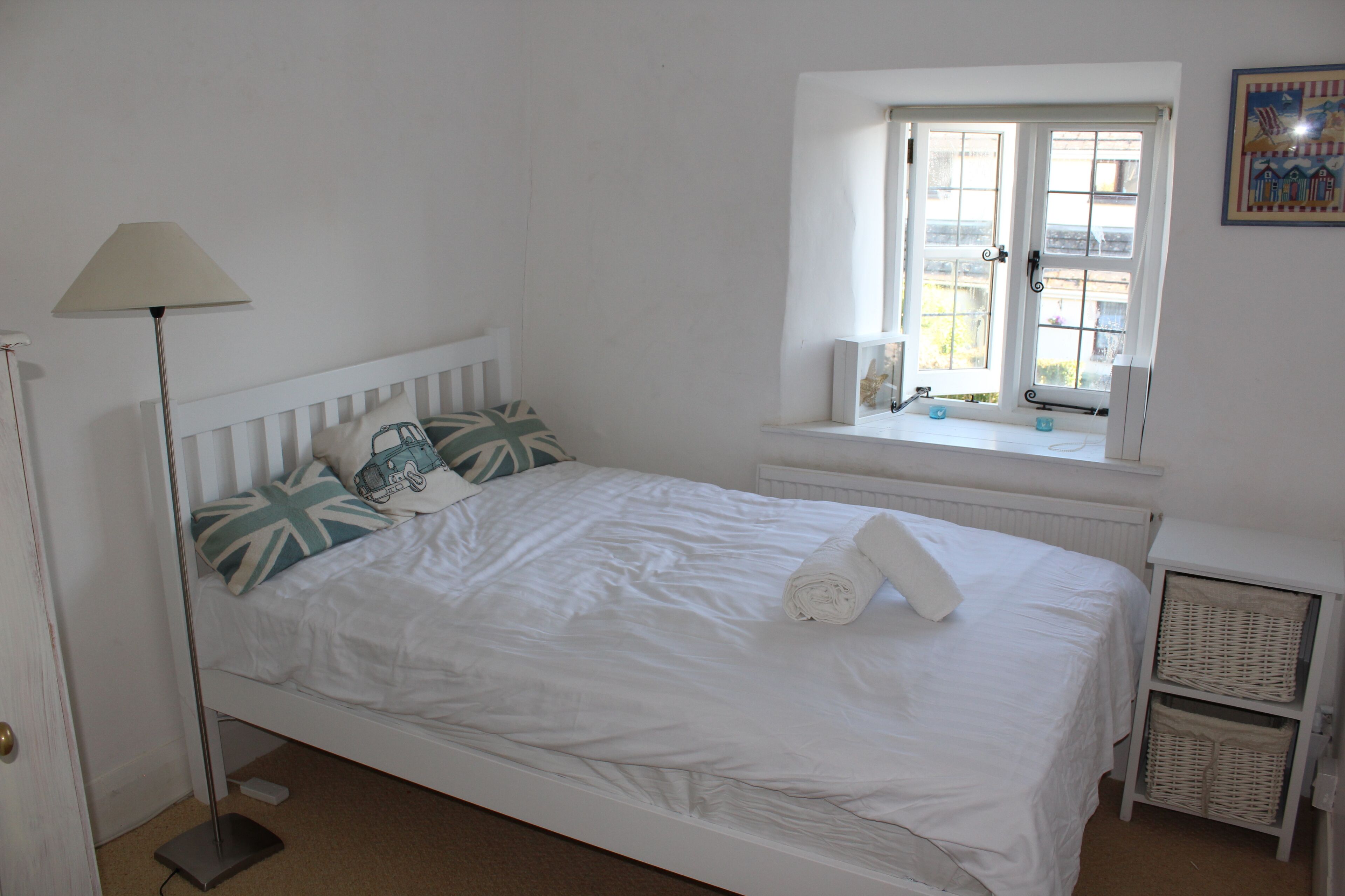 Una cama blanca con almohadas, una lámpara de pie, una ventana con vistas y un radiador.