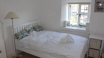 Una cama blanca con almohadas, una lámpara de pie, una ventana con vistas y un radiador.