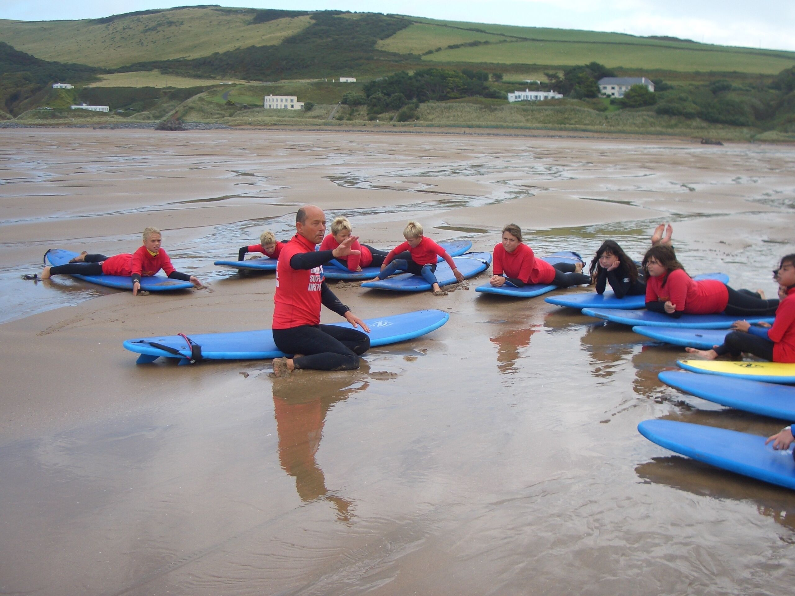 Un grupo de personas con trajes de neopreno rojo sobre tablas de surf azules en una playa mojada.