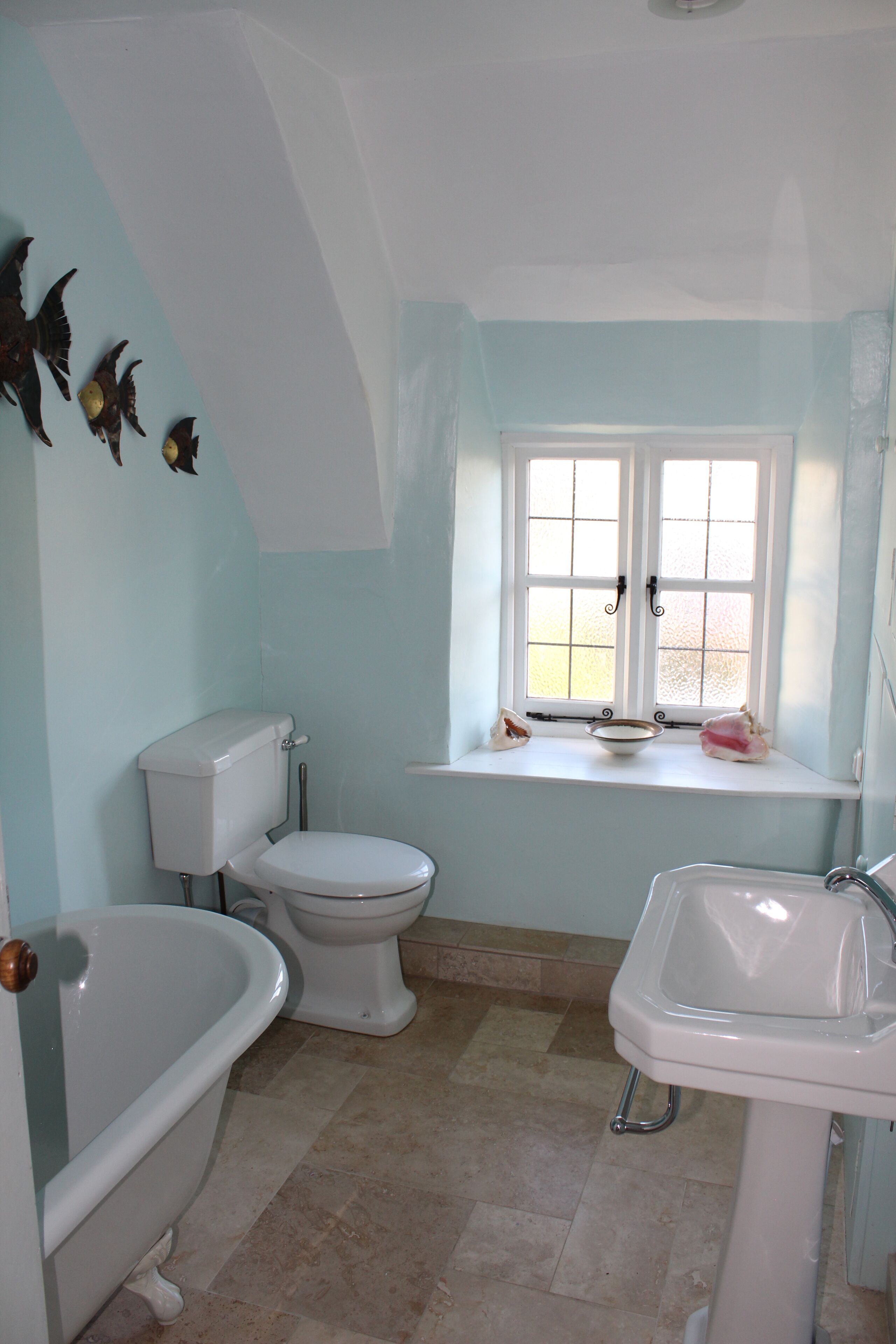 Ein Badezimmer mit Badewanne, Toilette und Waschbecken, mit einem Fenster und Ausblick nach draußen.