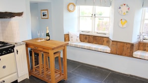 Una cocina con una mesa de madera, un rincón con asientos junto a la ventana y un reloj de pared.