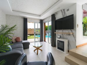 Una sala de estar moderna con un sofá, una mesa de centro de vidrio, una chimenea y un televisor montado en la pared.