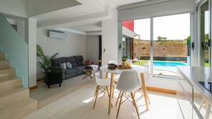 A modern living room with a sofa, dining table, and chairs, a staircase, and a view of a swimming pool. - Bali Sky Villa with Private Pool (San Bartolomé de Tirajana)