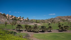 A golf course with palm trees, a clear sky, and buildings in the background. - Bali Sky Villa with Private Pool (San Bartolomé de Tirajana)