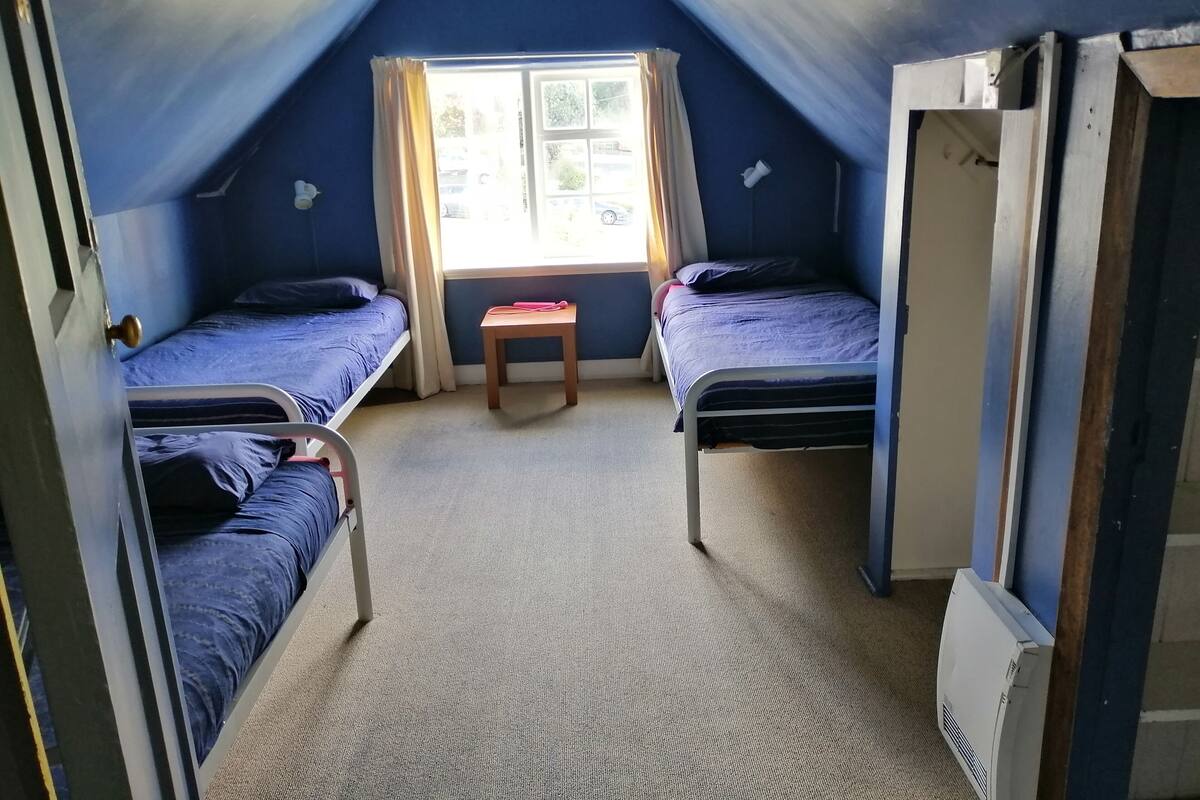 Una habitación con dos camas individuales, una mesita y un ventanal con cortinas.