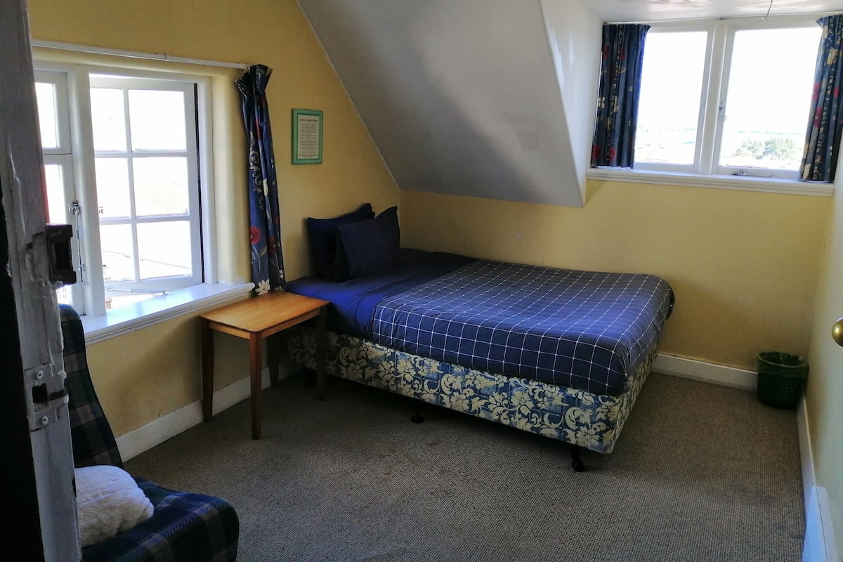 Una habitación pequeña y triangular con una cama, un escritorio y una ventana.