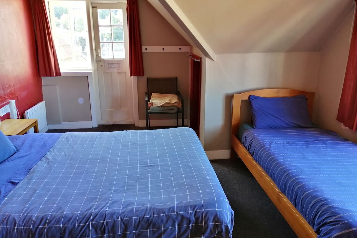 Un dormitorio con dos camas, una ventana con cortinas, un radiador y una silla.