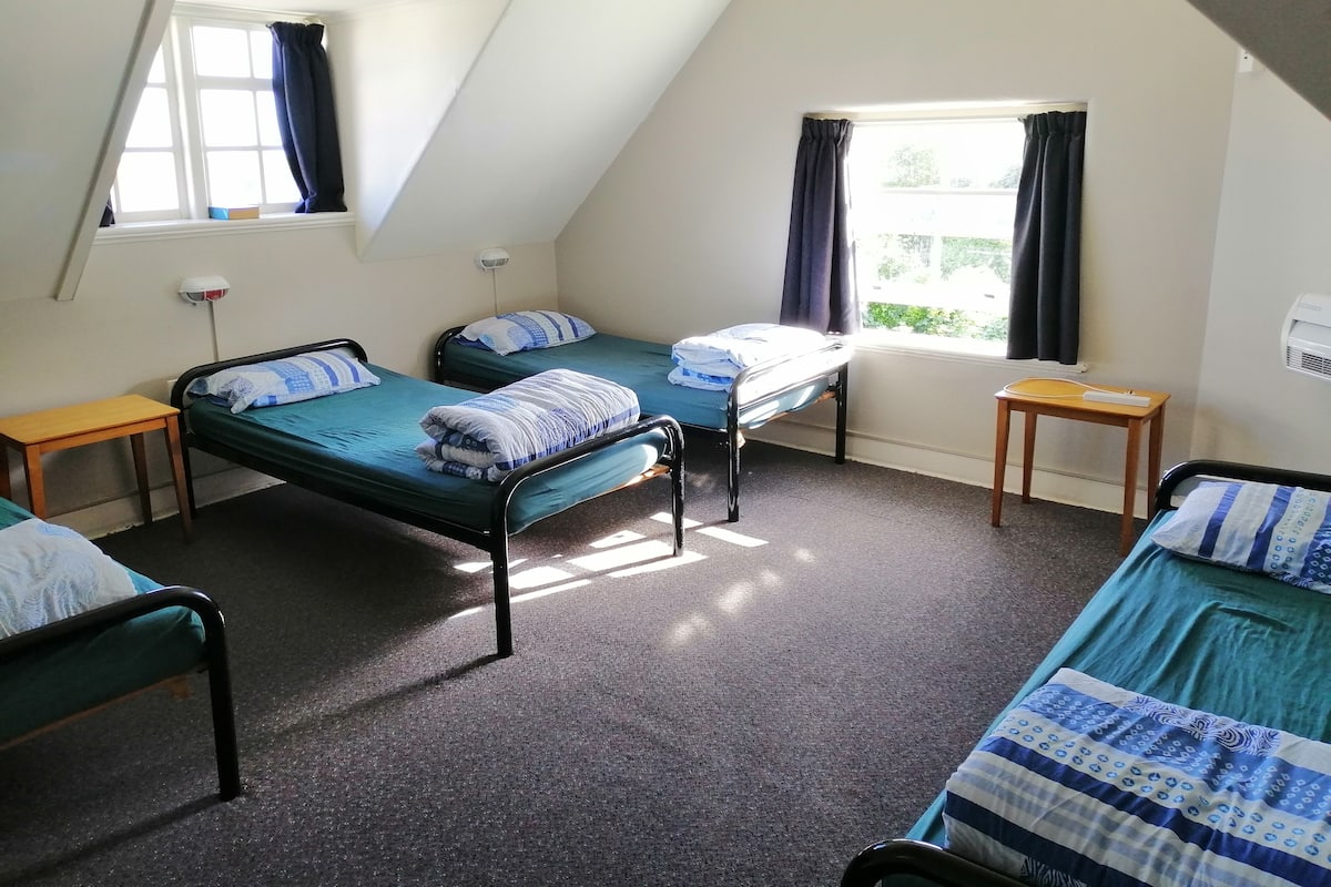 Un dormitorio con tres camas individuales, una mesita de madera y una ventana con cortinas.