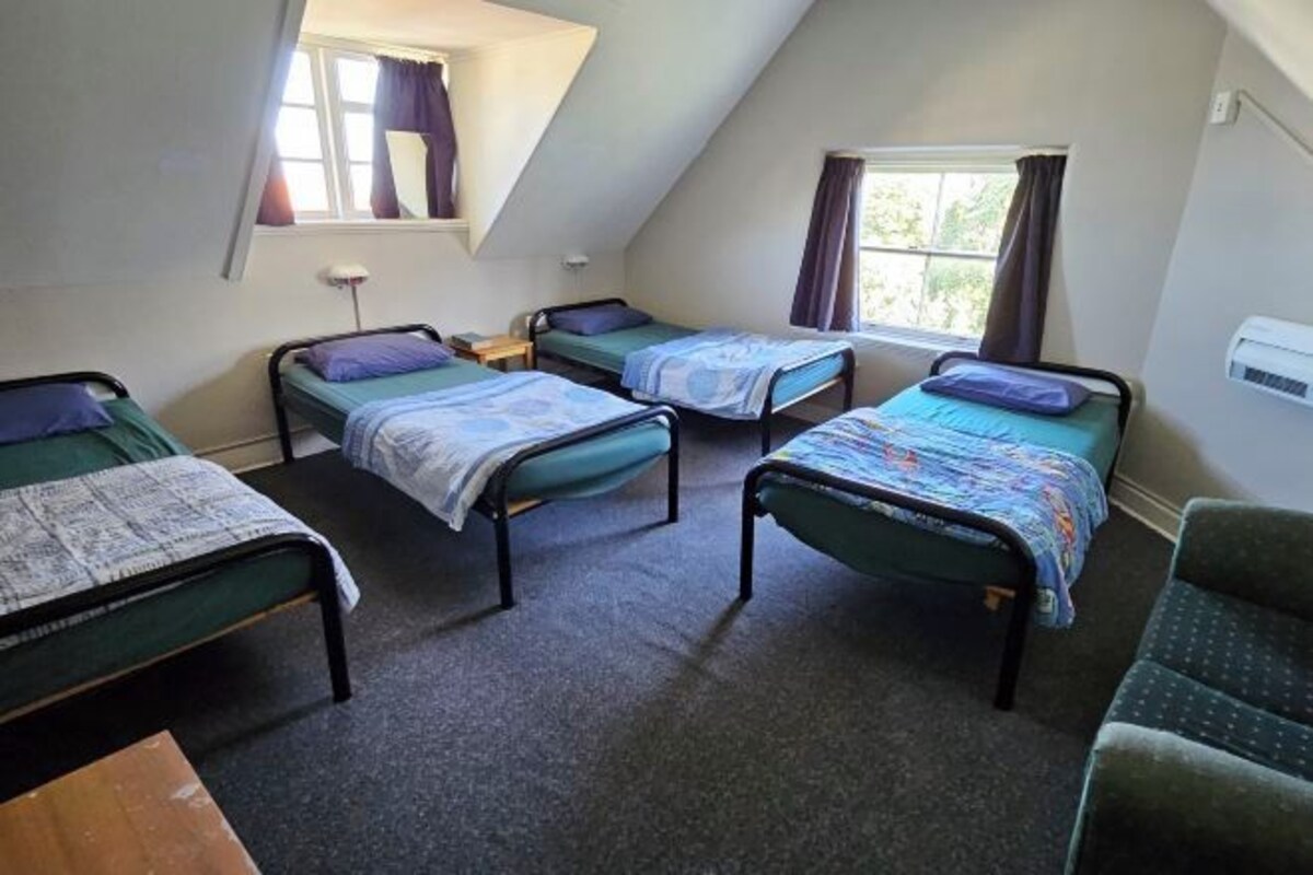 A dormitory room with four single beds, a small table, and a window with curtains.