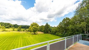 A view from a balcony overlooking a well-maintained lawn with a wooden deck and metal railing.