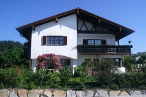 A two-story house with a white exterior, brown shutters, and a balcony with plants.