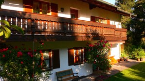 Un bâtiment à deux étages doté d’un balcon, de fenêtres avec volets et d’un banc à l’extérieur.