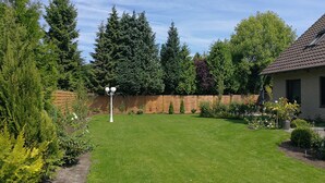 Een verzorgde achtertuin met gazon, houten omheining en diverse planten en bomen.