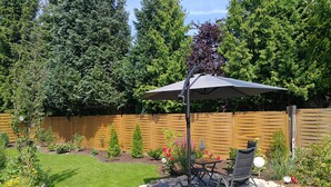Een terras met een tafel en stoelen onder een overkapping, omgeven door een tuin met verschillende planten en bloemen.
