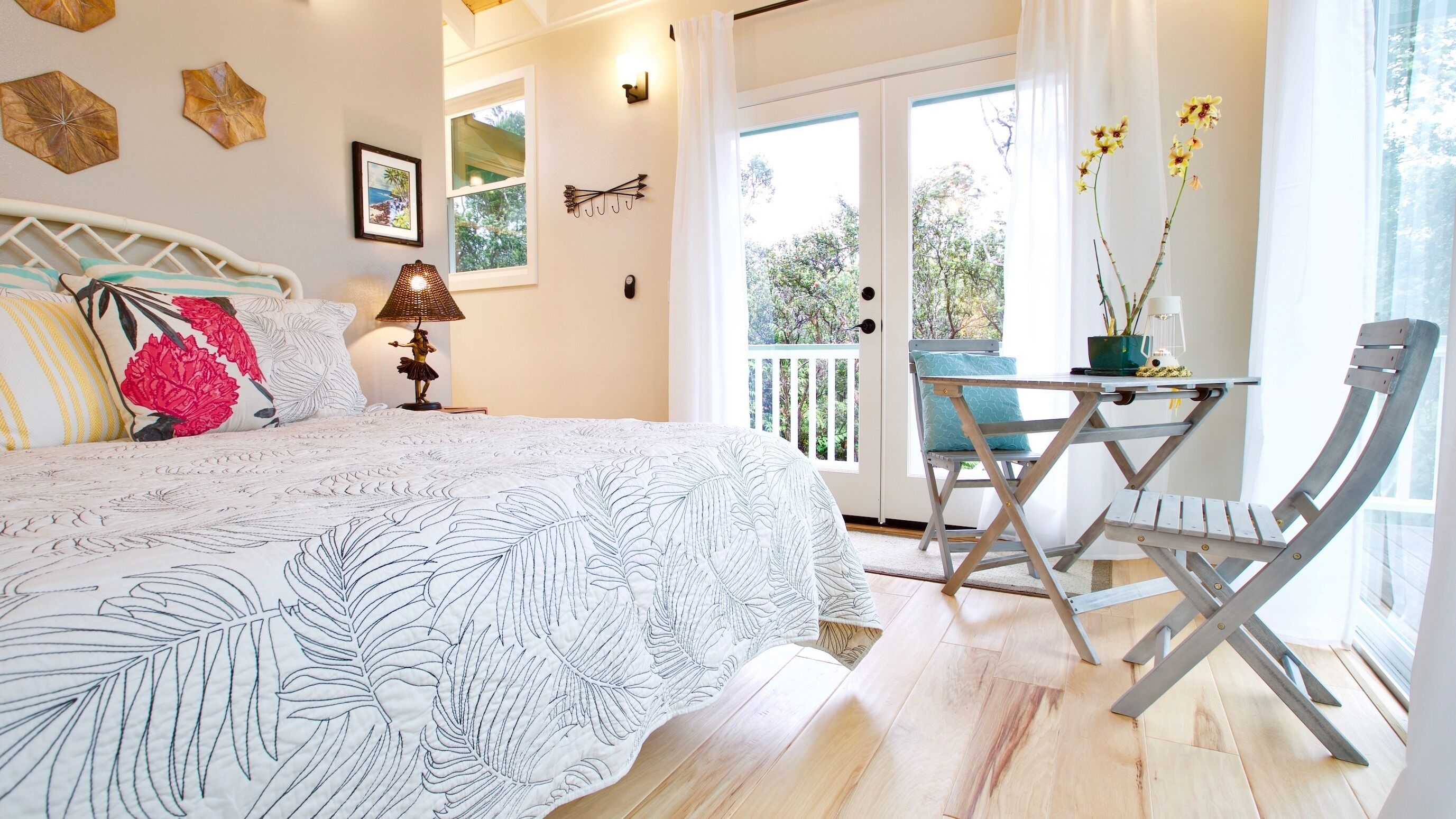Un dormitorio con cama, mesita de noche, lámpara, ventana con cortinas, balcón y una mesa con sillas.