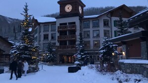 A multi-story building with a prominent clock tower, surrounded by snow-covered trees and a snowy ground.