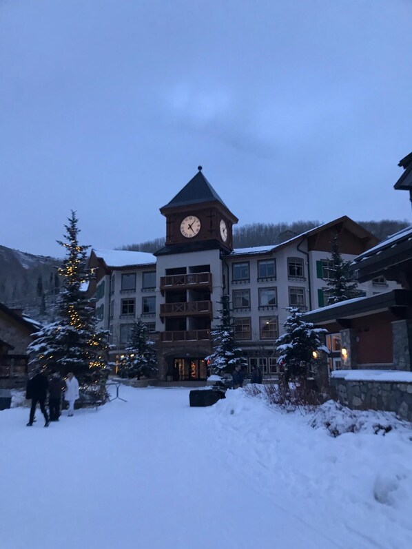 A multi-story building with a prominent clock tower, surrounded by snow-covered trees and a snowy ground.