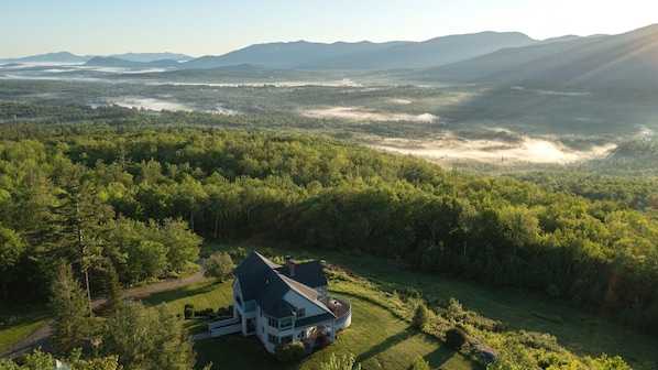 A large house surrounded by dense forest and mountains.