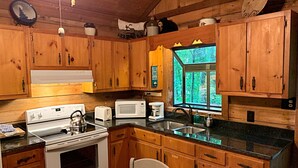 A wooden cabin kitchen with a stove, microwave, toaster, and a window with a view of trees. - Secluded cabin in Aska Adventure Area  (Blue Ridge)