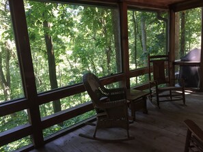 A wooden deck with a rocking chair and a table, overlooking a forest. - Secluded cabin in Aska Adventure Area (Blue Ridge)