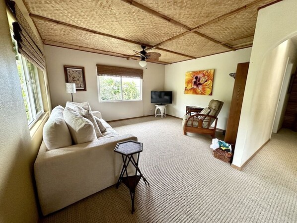 A spacious living room with a sofa, a small table, a TV, and a ceiling fan. - 5 Minutes to Beach & Town-Perfect Location, Private & Peaceful. A/C. (Kailua Kona)