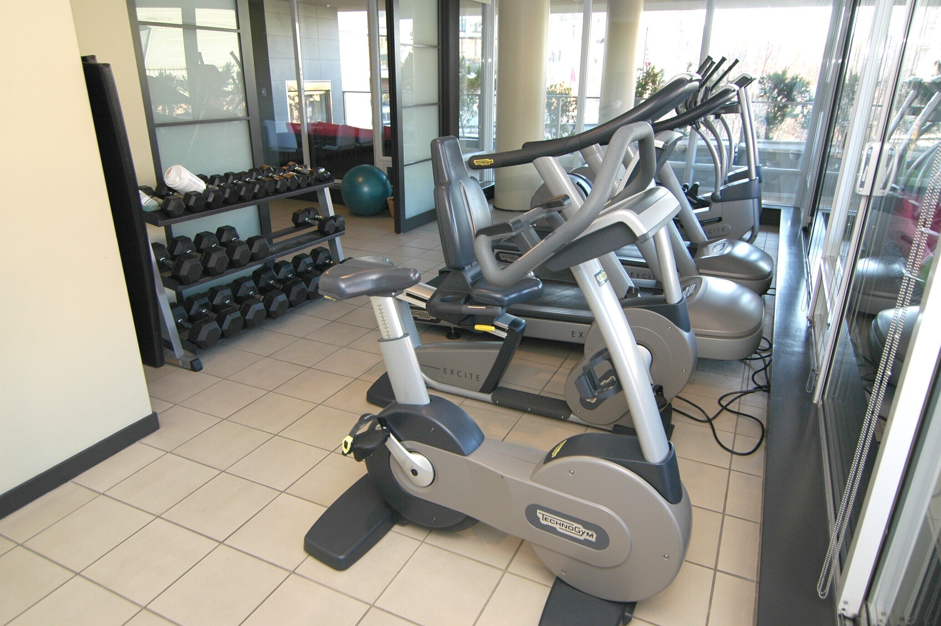A gym with exercise machines, dumbbells, and a large window.