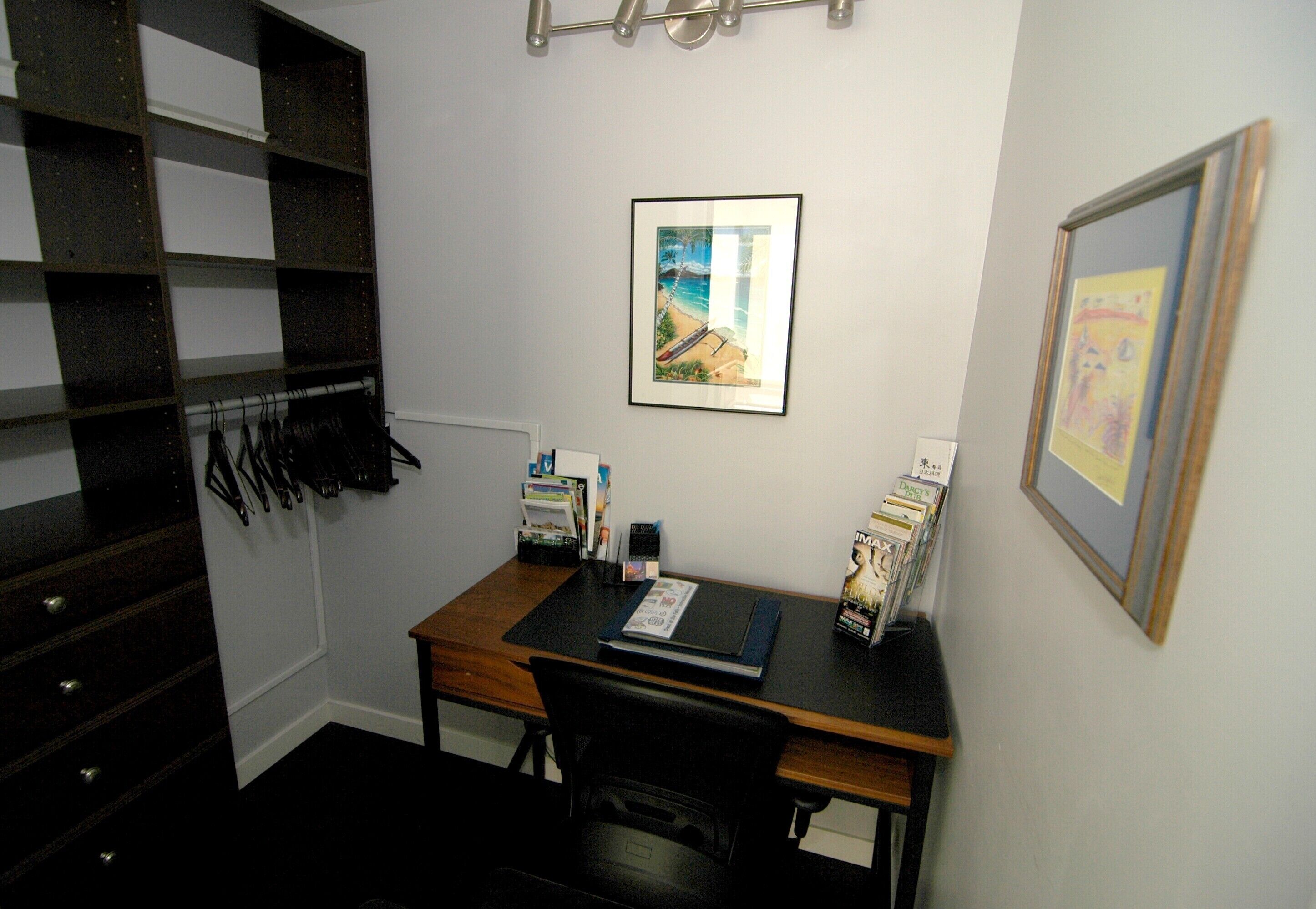 A room with a desk, chair, books, and framed pictures on the wall.