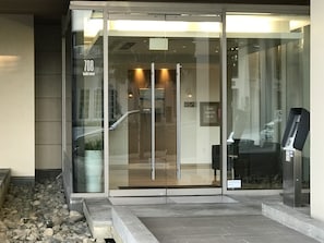 A modern building entrance with a glass door, a fire safety plan sign, and a visible address sign.