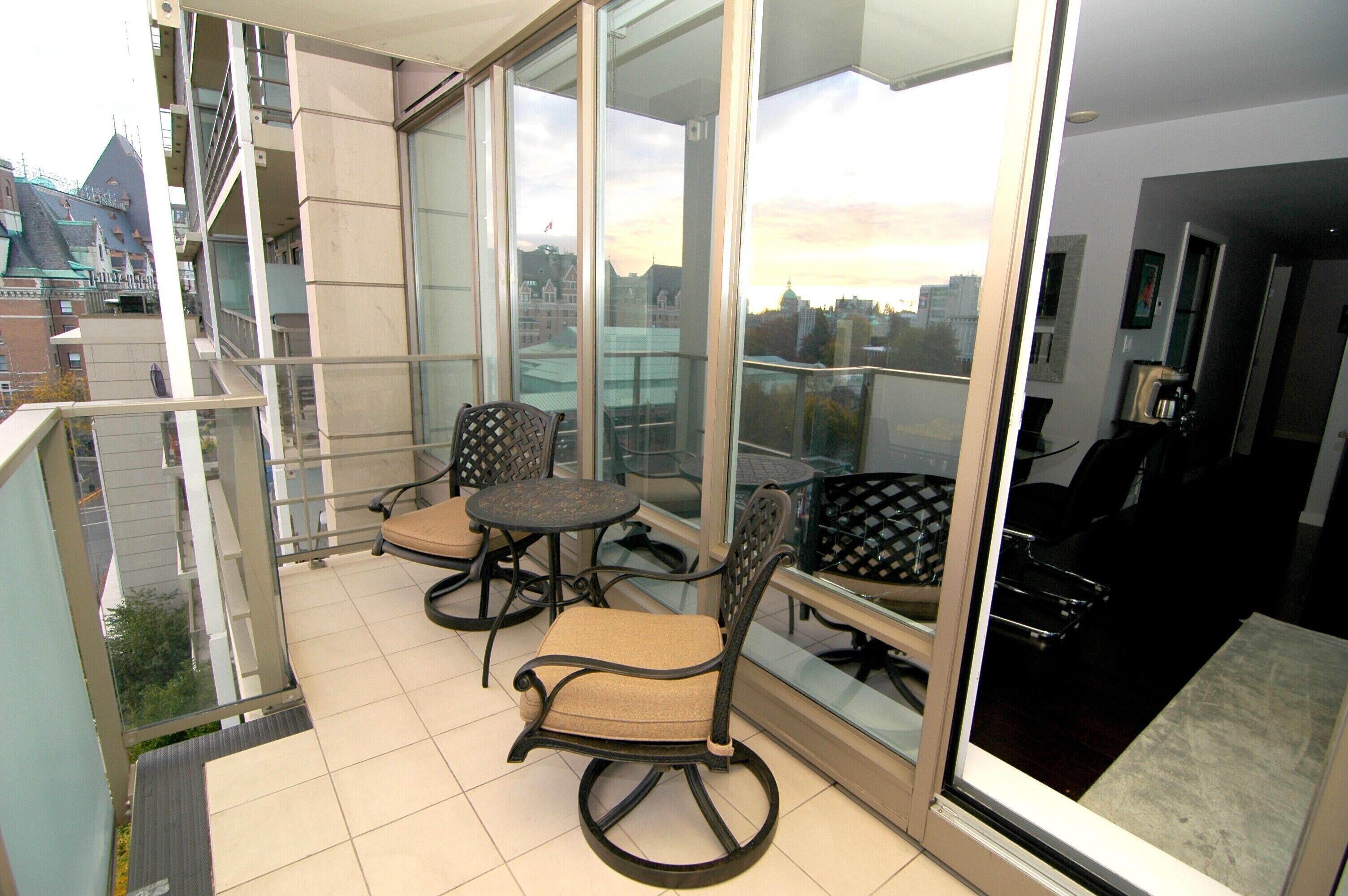 Un balcone con due sedie e un tavolino, ampie finestre con vista sulla città e una porta vetrata che dà accesso alla stanza.