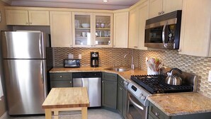 A modern kitchen with stainless steel appliances, a wooden table, and a tiled backsplash.