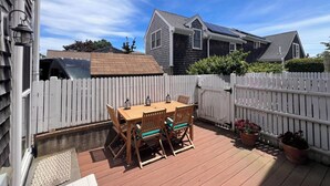 A deck with a table and chairs, a white picket fence, and a house with solar panels in the background.