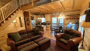 A cozy cabin interior with a wooden staircase, a dining area, and a living room with a sofa and ottoman.