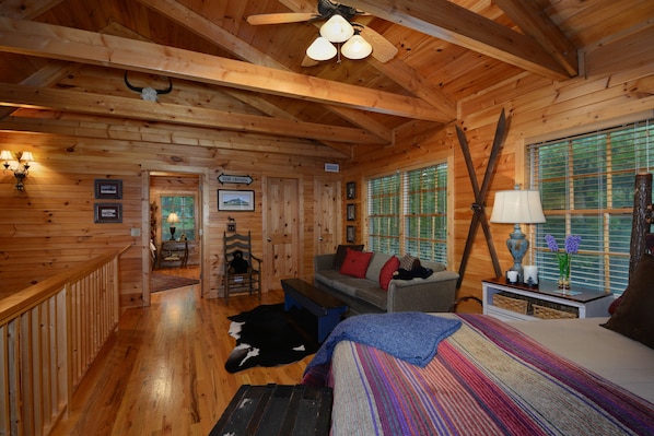 A log cabin interior with wooden walls, a bed, a sofa, and a dining area.