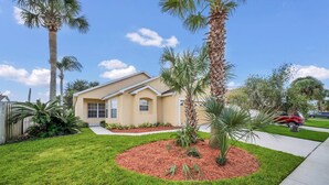 A single-story house with a well-maintained lawn, palm trees, and a driveway.