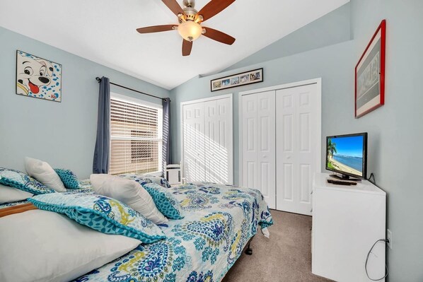 Un dormitorio con una cama, ventilador de techo, televisor y armario.
