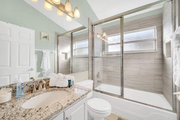 A bathroom with a glass-enclosed shower, a sink with a granite countertop, and a toilet.