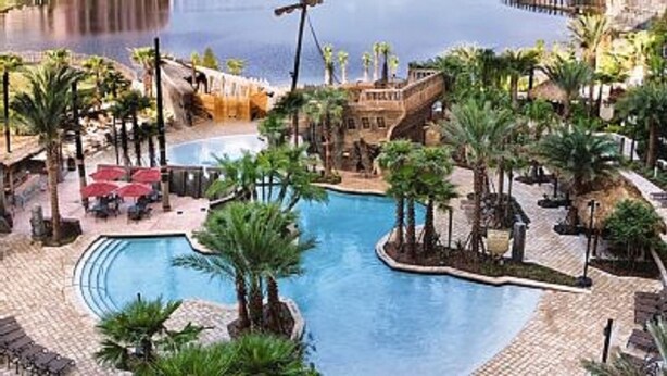 A resort pool area with a central pool, palm trees, and a bridge connecting different sections. - Minutes away from all the fun at Disney Resorts!  Everything you need and want! (Orlando)