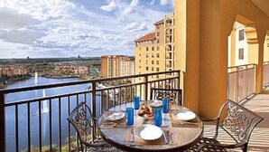 A balcony with a table set for two, overlooking a body of water and buildings. - Minutes away from all the fun at Disney Resorts!  Everything you need and want! (Orlando)