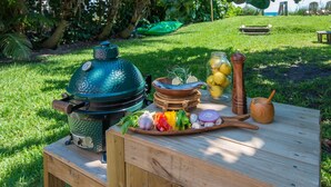Ein Holztisch mit einem tragbaren Grill, einer Holzschüssel mit Zitronen, einer Gewürzmühle, einem Holzlöffel und einer Holzschüssel mit geschnittenem Gemüse.